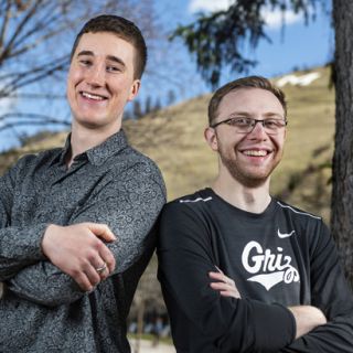 Recent UM graduates Noah Grabe, left, and Taylor Gregory, right, stand back-to-back on campus.
