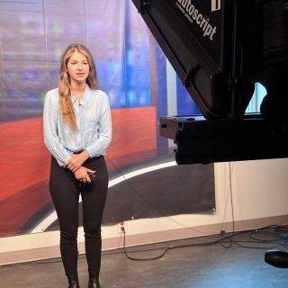 Woman with brown hair looking at camera in TV studio.