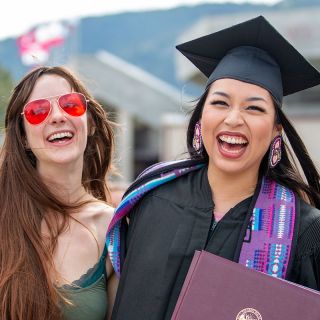 A graduating student smiles as she embraces friends in a side-hug