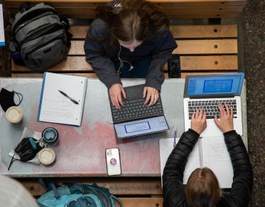 Image of students on their laptops sitting at a table.