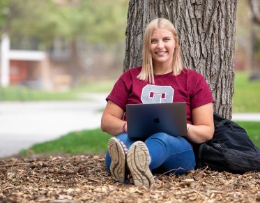 Student sitting against a tree using a laptop