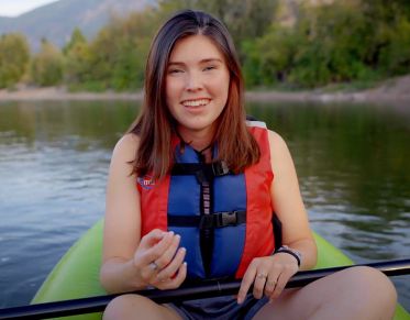 UM student Arwen Baxter looks at the camera and speaks while sitting in an inflatable kayak in the river