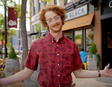 UM student John Shelton looks at the camera and gestures with his hands while speaking as he stands on Higgins Avenue in downtown Missoula.