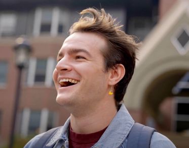 UM student Josh Martelon looks to his right and smiles while standing in front of Pantzer Hall at UM.