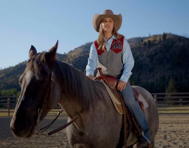 UM student Lauren Johnson speaks at the camera while sitting on her horse in the rodeo practice arena.