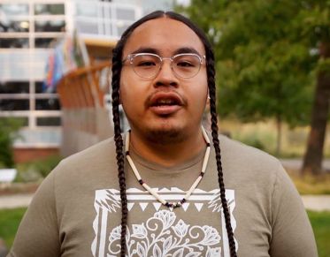 UM student Zachariah Rides at the Door speaks at the camera while standing in front of the Payne Family Native American Center.