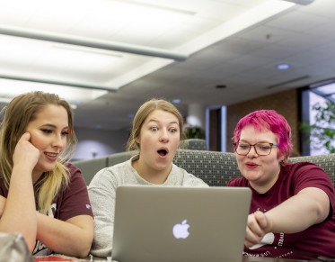 Three students using a laptop looking surprised