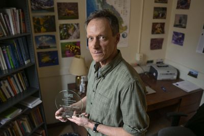 A picture of Christopher Preston holding his award in his UM office.
