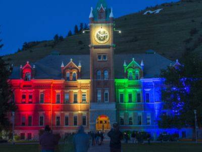 main hall building on the university of montana campus lit up by rainbow colored lights at night