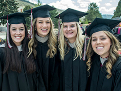 Four female graduates smiling and posing together in their caps and gowns at a graduation ceremony