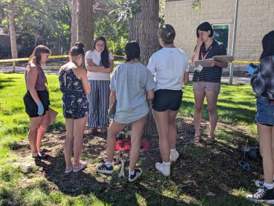 a group of students listens to an instructor by a plastic skeleton on the ground