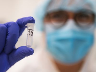 person wearing mask and protective gear holding a vial