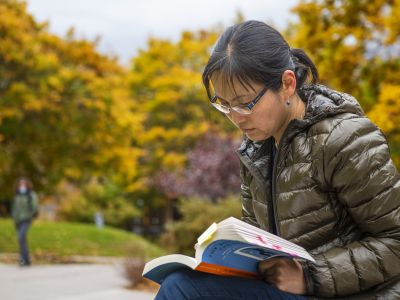 Student studies among the bright amber trees near Main Hall