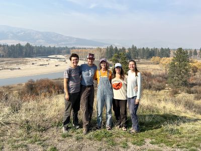 Five biologists smile at the camera with a vista of mountains and the Bitterroot River behind them.