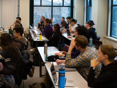 three rows of students along tables looking left to the front of the class