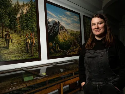 Student standing in front of paintings of a forests