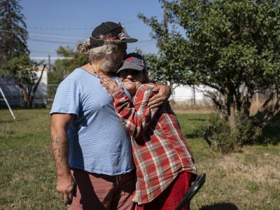 Man in blue shirt hugs woman in plaid shirt.