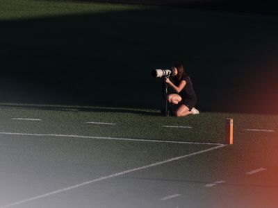 Woman with camera crouches near a football endline.