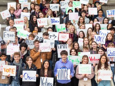 A group of highschool students smiling holding signs