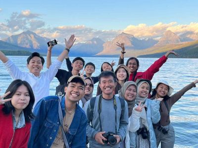 A group of diverse students posing joyfully by a lake with mountains in the background
