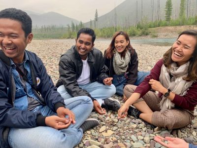 A group of four students laughing and sitting on a rocky riverbank