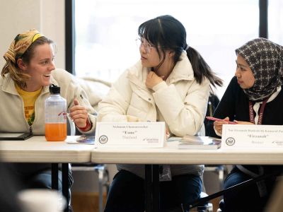 Three people engaged in discussion at a roundtable meeting, with nameplates identifying their countries: Thailand, Brunei, and another participant