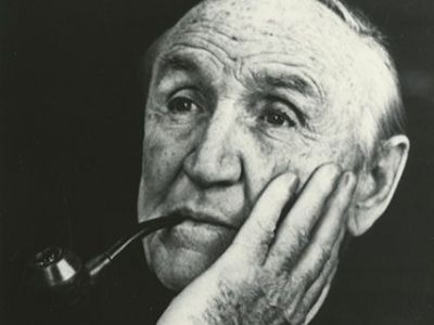 Mike Mansfield in a black and white photograph smoking from a pipe while staring off into the distance. He appears to be deep in thought.