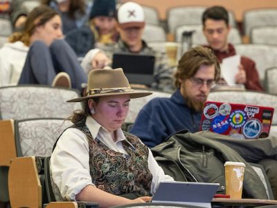 Students sit in chairs looking at laptops