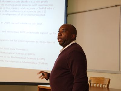 Edray Goins talks in front of projector screen 