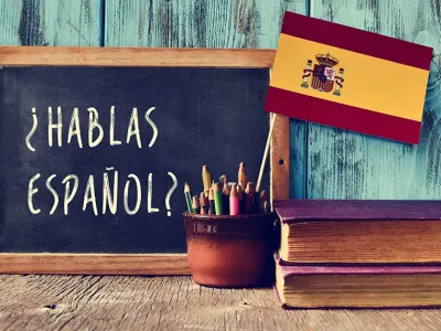 hablas espanol on a chalkboard on a desk with books and a flag