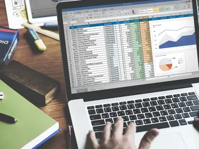 hands working on a laptop in excel on a messy desk