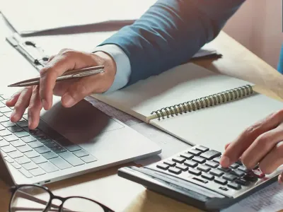 one hand working on a laptop with the other on a calculator