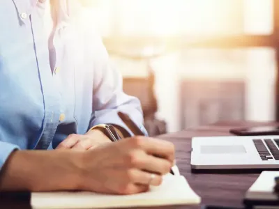 hand writing in a notepad in front of a laptop