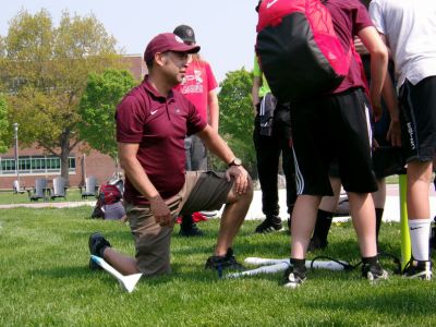 A role model kneels in grass as they demonstrate a rocket-launching activity to a group of middle school students.