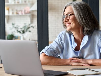 Photograph of 60 year old woman in front of laptop with the button title "Trainings"