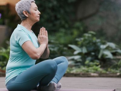 Photo of 70 year old woman in yoga pose on a yoga mat, links to "Wellness"