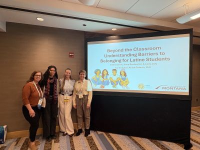 Three graduate students and a professor standing in front of a conference presentation screen