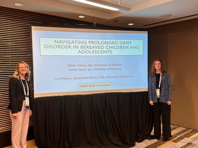 Two graduate students, Gillian and Caitlin, standing in front of a screen at a conference presentation