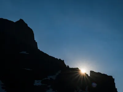 Sun peaking over a rocky mountain top in Glacier National Park.
