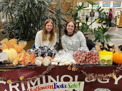Crim Club students sitting at a table full of bake sale treats to raise money.
