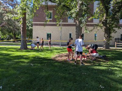 Groups of students outside surrounded by caution tape while investigating something on the ground.
