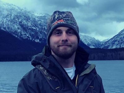 Zach Rehm standing along a lake backed by snow-capped mountains