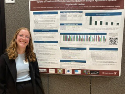 a student stands in front of her research poster