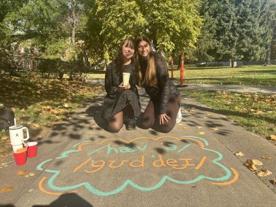 two students pose on their knees in front of a chalk phrase that is the phonetic alphabet for "have a good day"