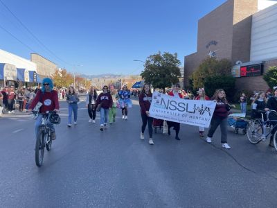 a group of students in a parade walk down the street holding a nsslha sign