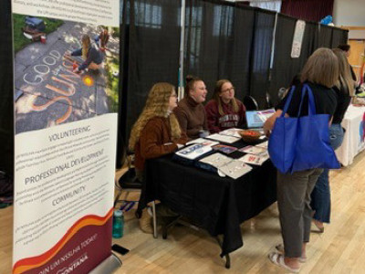 three students table at a conference. a large vertical banner on the left designates the table as NSSLHA
