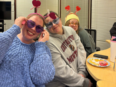 three students smile for the camera. the front and back have springy heart ear head bands. the first and second have fun blue glasses
