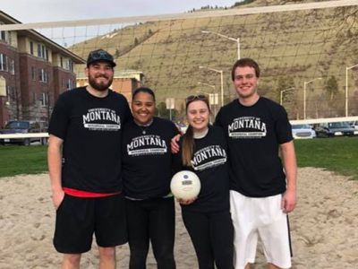 Four members of a sand volleyball team pose on the court for a photo