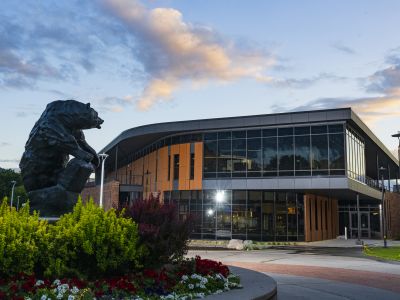 behind the grizzly bear statue, the lodge is lit by the rising sun on UM's campus