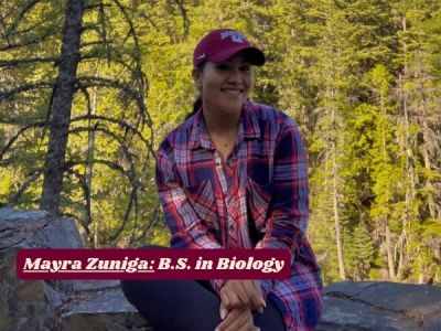 Mayra smiles while sitting on rock, dense forest in background